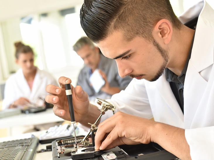Egy fiatal fiú köpenyben a munkaasztal fölé hajolva precíz munkát végez