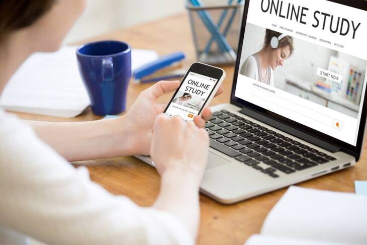 Laptop és mobiltelefon előtt ülő tanuló online tanul