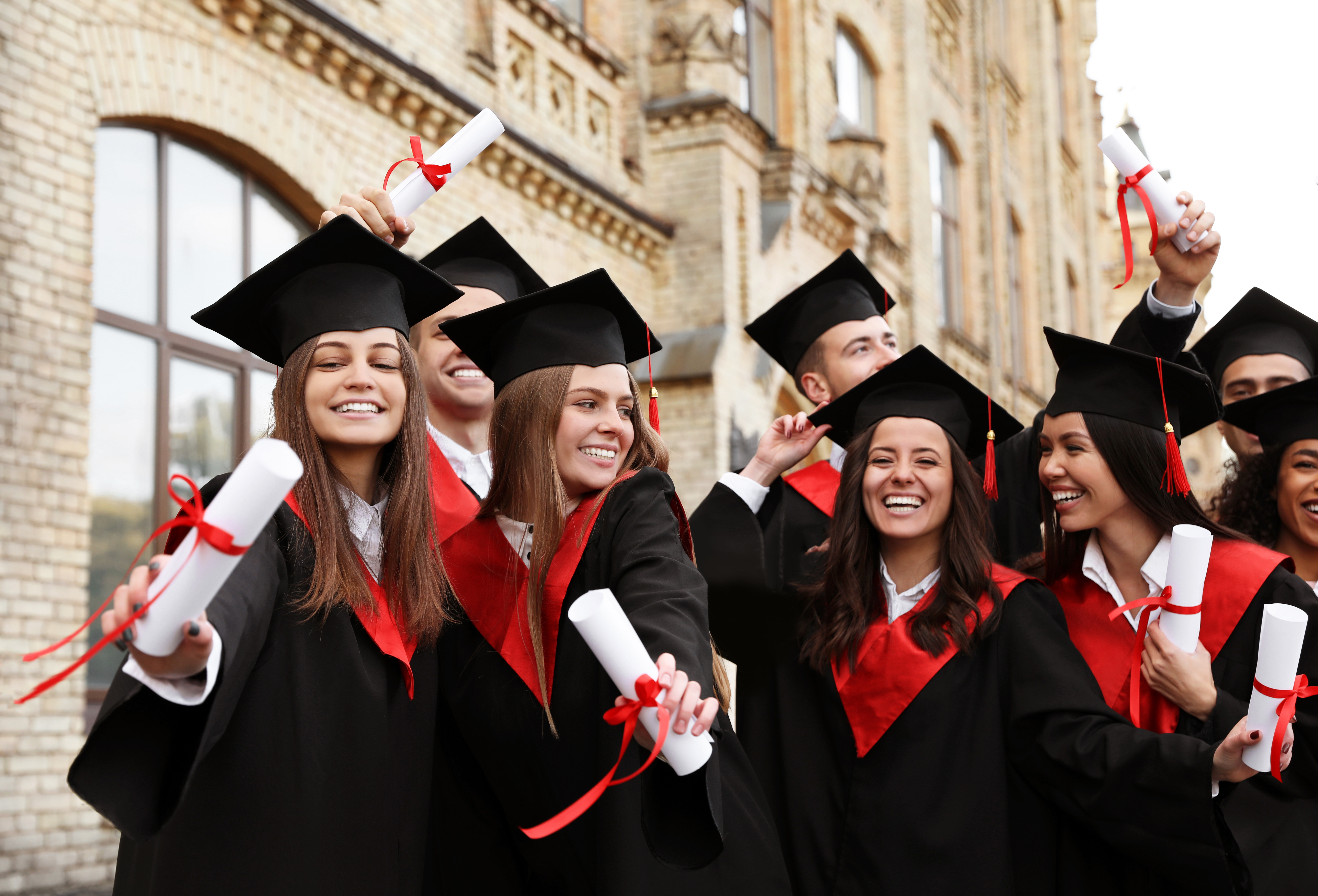 Diplomaosztó ünneplése egy csapat taláros mosolygó fiatal áll bölcsész sapkában és az oklevelükkel a kezükben
