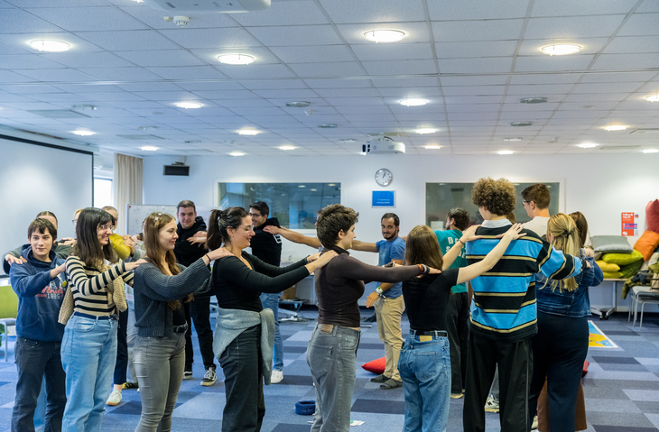 DiscoverEU After utazás utáni találkozó közös játékában a résztvevők egymás vállát fogva állnak körben egy teremben
