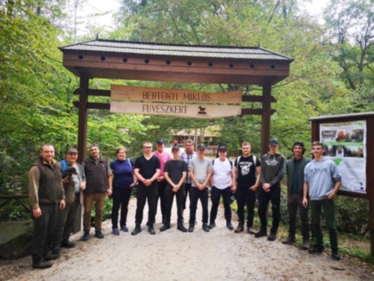 Finn és magyar diákok és oktatóik állnak az erdőben a Bertényi Miklós Füvészkert tábla alatt