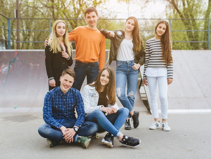 fiatal fiúk és lányok egy gördeszka pályán a kamerába néznek