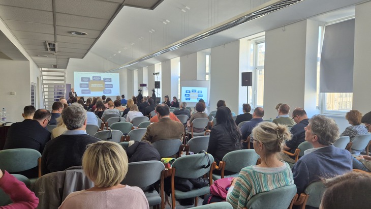 Egy tágas teremben széksoros elrendezésben ülő hallgatók figyelik az előadót