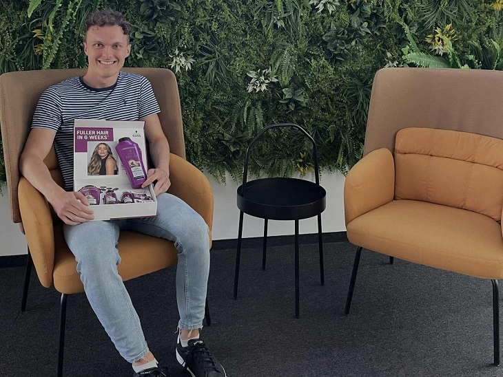 Fiatal egyetemista férfi csíkos pólóban sárga kanapén ül egy növényfal előtt