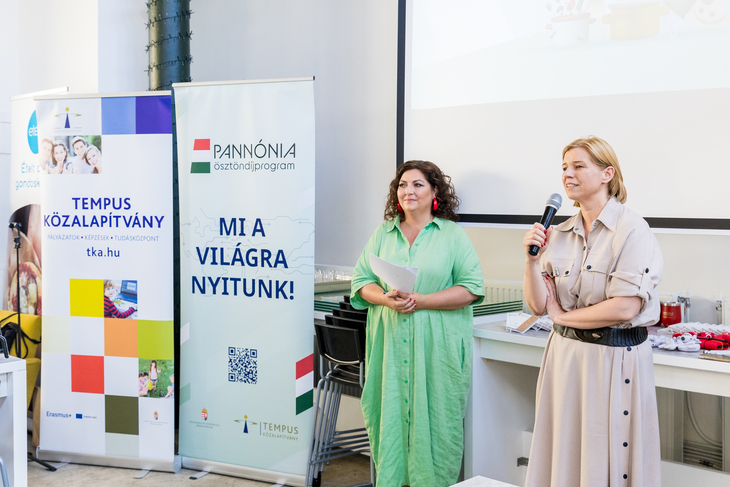 Pannónia Alumni klub bevezető beszéd Dr Varga Bajusz Veronika és Mautner Zsófi állnak 2 promóciós háttérfal mellett