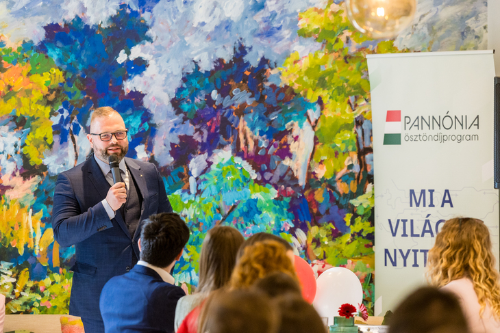 Bodrogi Richárd a Tempus Közalapítvány főigazgatója beszél a hallgatóságának egy színes fal és a Pannónia plakátja előtt
