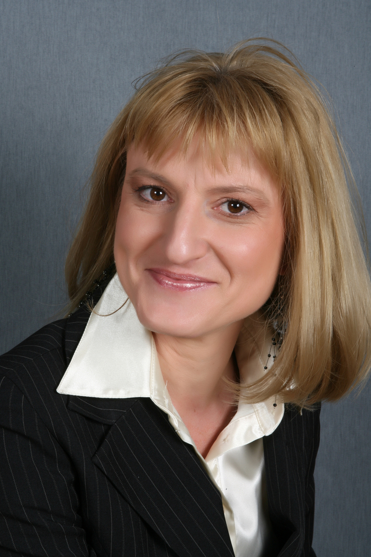 Szőke hajú barna szemű hölgy fehér ingben és fekete zakóban