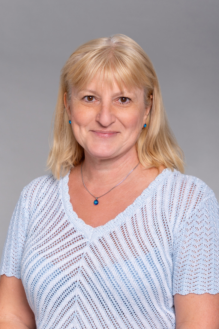 Szőke hajú barna szemű hölgy fehér ingben és fekete zakóban