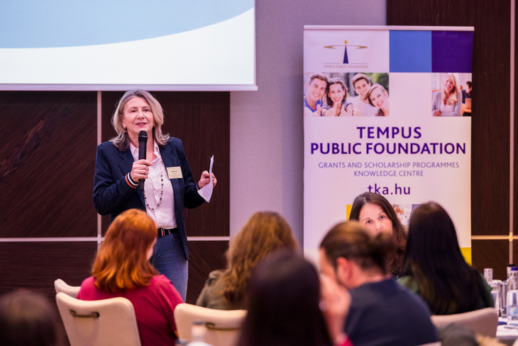 Sötétkék zakóba öltözött hölgy előadást tart kivetítő előtt