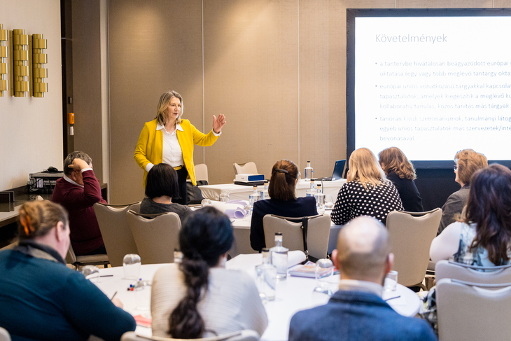 sárga zakóba öltözött hölgy előadást tart kivetítő előtt