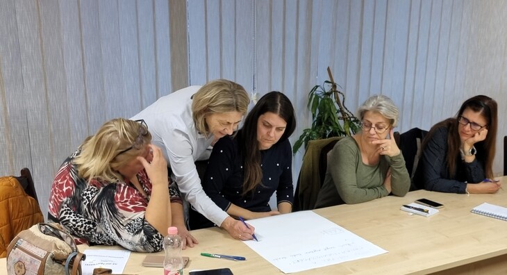 5 hölgy egy asztalnál közösen néz egy A3as méretű papírlapot
