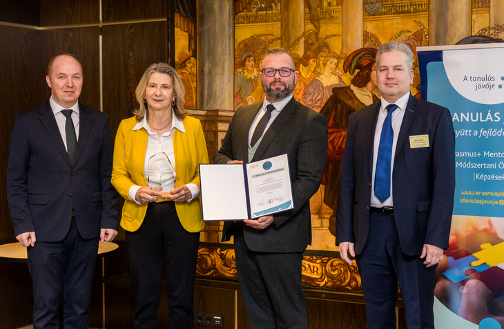 Három öltönyös férfi gratulál egy sárga zakóba öltözött nőnek A Tanulás Jövője Díj átvételéért