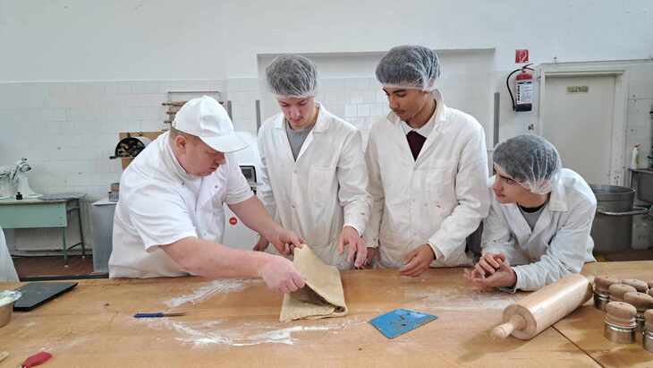 Hajh&aacute;l&oacute;ban &eacute;s feh&eacute;r k&ouml;penyben h&aacute;rom szak&aacute;cs tanonc figyel egy feh&eacute;rbe &ouml;lt&ouml;z&ouml;tt oktat&oacute;t