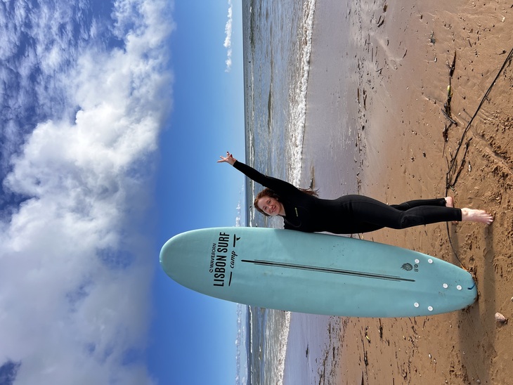 Vada Virág egy szörfdeszkával áll a homokos parton