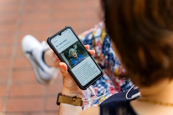 Egy hölgy az okostelefonján videóinterjút néz és hallgat